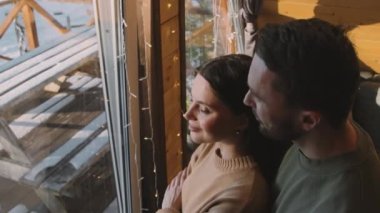 Yüksek açılı, neşeli bir adamın kamarada dikilip kış gününün tadını çıkarırken karısına yaklaşması. Ona sarılıyor ve sevgiyle gülümsüyor.