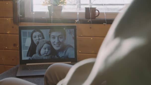 手持慢镜头的难以辨认的男子在视频通话与快乐的亚洲家庭与小孩 阳光明媚的日子里 笔记本电脑靠窗躺在沙发上 — 图库视频影像