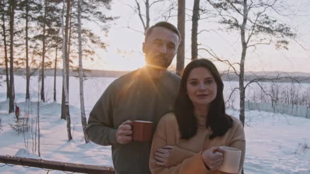 男性と女性が熱いお茶のカップを保持し 冬の夜に彼らのキャビンの前のポーチにポーズの手持ちの肖像画 — ストック動画