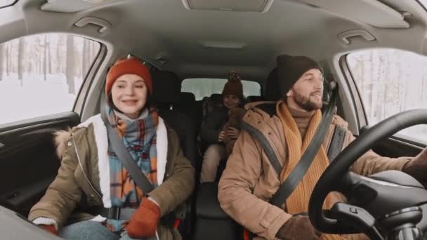 移動中の車の中から撃たれた幸せな男が運転し 冬に森の中を旅しながら助手席と後部座席に座っている彼の妻とかわいい8歳の女の子とチャット — ストック動画