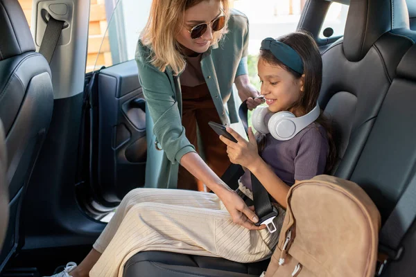 Jong wijfje helpen haar dochtertje met smartphone vast veiligheidsgordel — Stockfoto