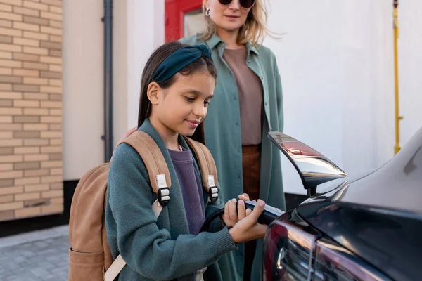 Klein meisje met rugzak helpen haar moeder opladen ev auto batterij — Stockfoto