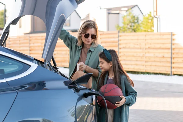 Klein meisje en jonge vrouw stand-by kofferbak van elektrische auto — Stockfoto