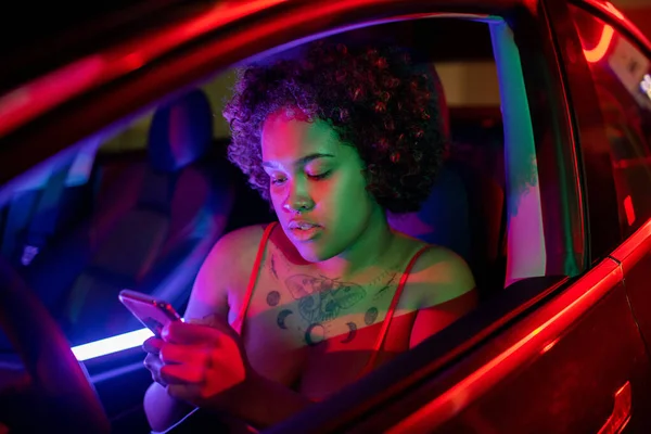 Hübsches afrikanisches Mädchen blättert beim Autofahren im Smartphone — Stockfoto