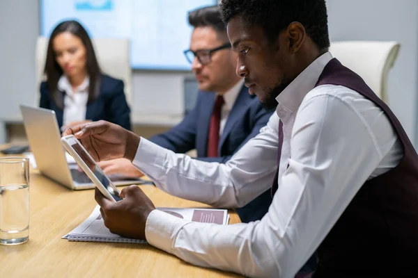 Hombre de negocios serio desplazándose en tableta contra compañeros de trabajo — Foto de Stock