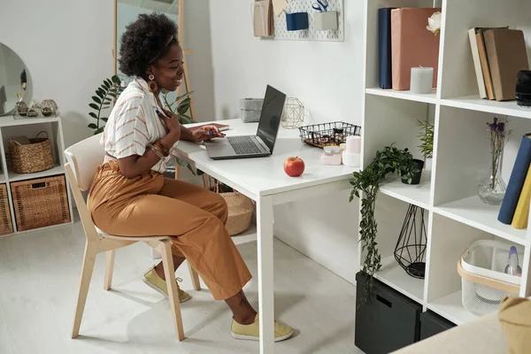 Glückliche junge Geschäftsfrau interagiert im Videochat, während sie am Schreibtisch sitzt — Stockfoto