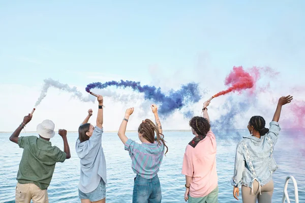 Cinq amis extatiques avec des pétards colorés s'amuser au bord de l'eau — Photo