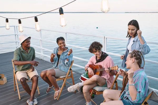 Jóvenes amistosos cantando con la guitarra mientras pasan tiempo en el muelle en el día de verano —  Fotos de Stock