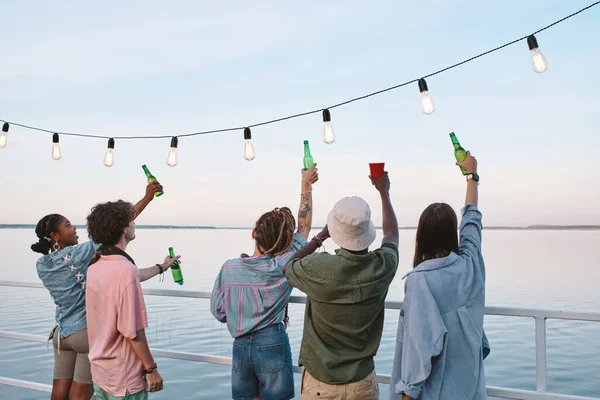 Vista trasera de los jóvenes amigos con bebidas disfrutando de la fiesta al aire libre —  Fotos de Stock