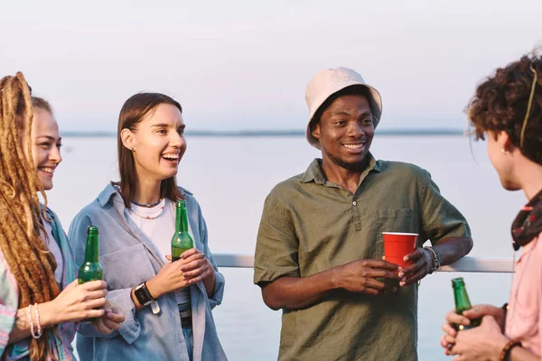 Jóvenes amigos alegres con bebidas contando chistes en la fiesta de verano —  Fotos de Stock