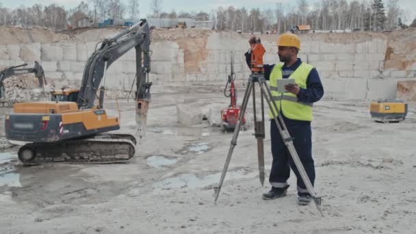 用测量仪器用石碑对阿拉伯男性花岗岩采石工人进行慢速跟踪 站在他旁边的钻机 — 图库视频影像