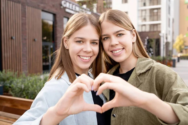 Glad tillgiven tvilling flickor gör form av hjärta med händer — Stockfoto