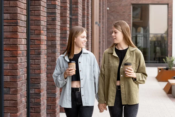 Twin girls interacting and having drinks while moving down street — Stock Photo, Image