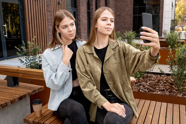 Güzel genç ikizler bankta otururken selfie çekiyorlar. — Stok fotoğraf