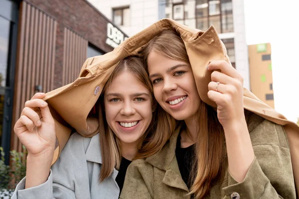 İki mutlu sarışın kız kafalarını trençkotla örtüyor. — Stok fotoğraf