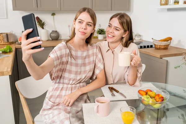 Šťastné dvojče dospívající dívky dělat selfie nebo video volání v kuchyni — Stock fotografie