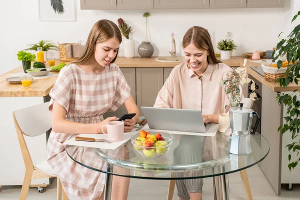Samtida tvillingflickor med mobila prylar vid köksbordet — Stockfoto