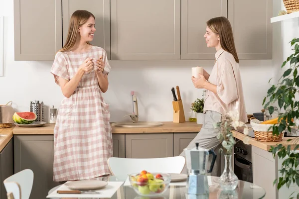 Atraktivní dospívající dvojčata s nápoji interagující v kuchyni — Stock fotografie
