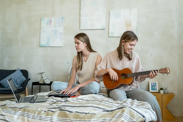 Tatlı genç kız ikiz kardeşinin gitar çalışını kaydediyor. — Stok fotoğraf