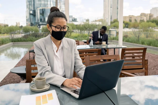 Jovem fêmea em máscara protetora digitando no teclado do laptop — Fotografia de Stock