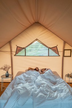 Çift kişilik yatakta beyaz battaniyenin altında uyuyan genç çift.