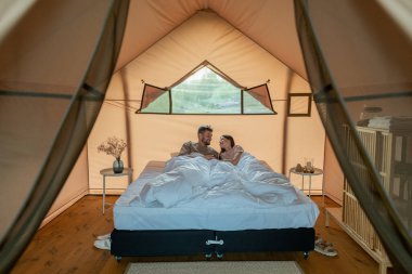 Amorous çifti glamping evinde çift kişilik yatakta dinleniyor.