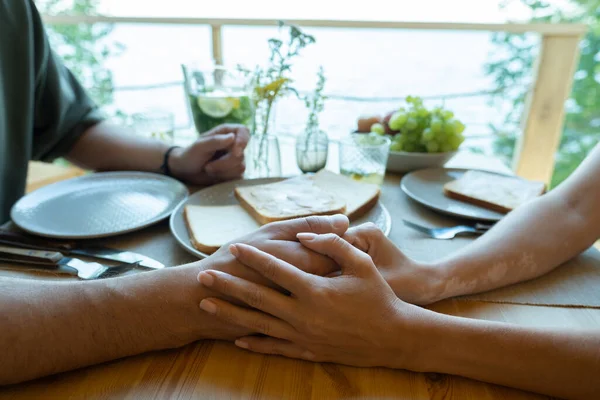 Handen van jong liefdevol paar zitten aan tafel geserveerd — Stockfoto