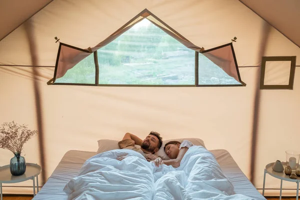 Νεαρός άνδρας και γυναίκα κοιμούνται σε μεγάλο διπλό κρεβάτι μέσα σε σκηνή glamping — Φωτογραφία Αρχείου