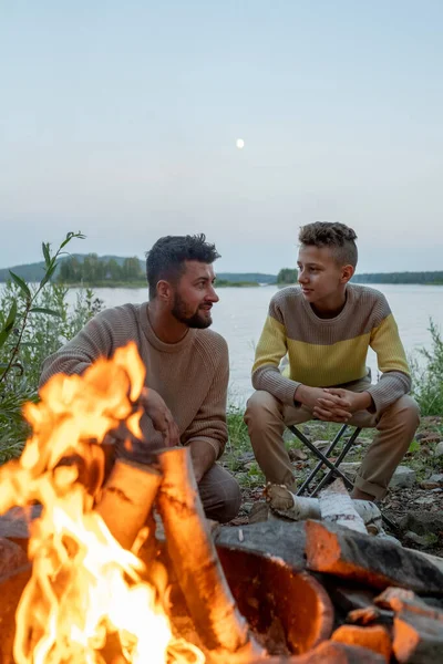 Junger Vater und Sohn sitzen abends am Lagerfeuer — Stockfoto