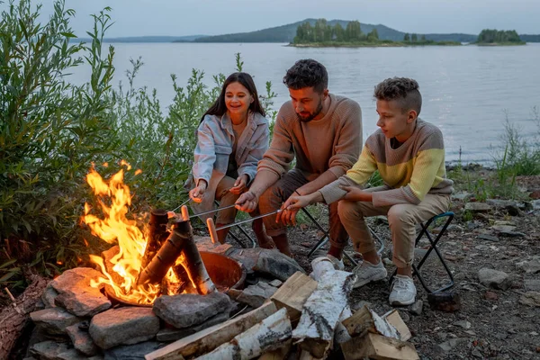 Familie junger Eltern und ihr Sohn braten Würstchen — Stockfoto