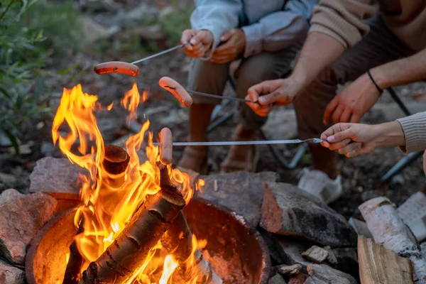 Ung familj med tre kokkorvar över lägerelden — Stockfoto