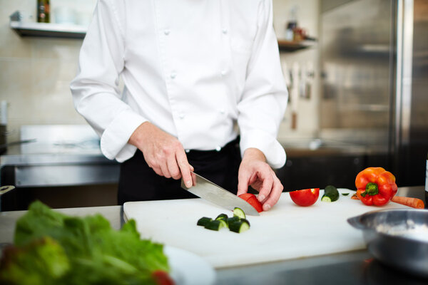 Image of male hand with knife cutting cucumber and tomato on wooden board