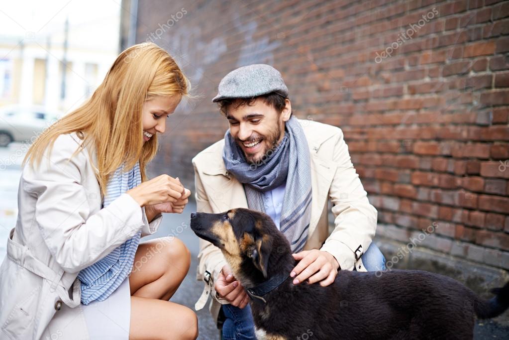 Happy young couple feeding dog
