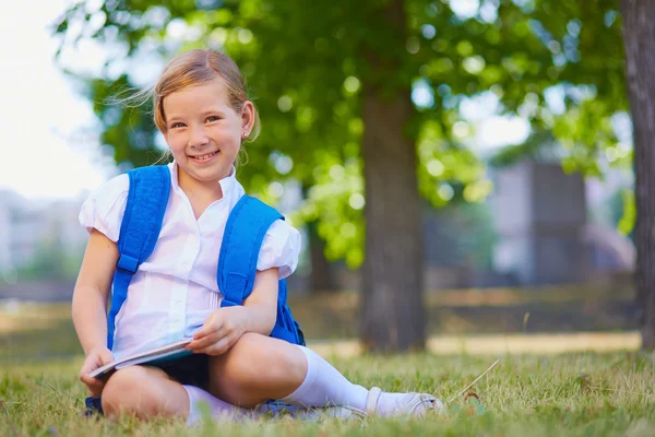 Child with backpack sitting on grass — Stock Photo, Image