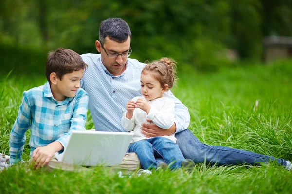 Homem e duas crianças usando laptop no parque — Fotografia de Stock