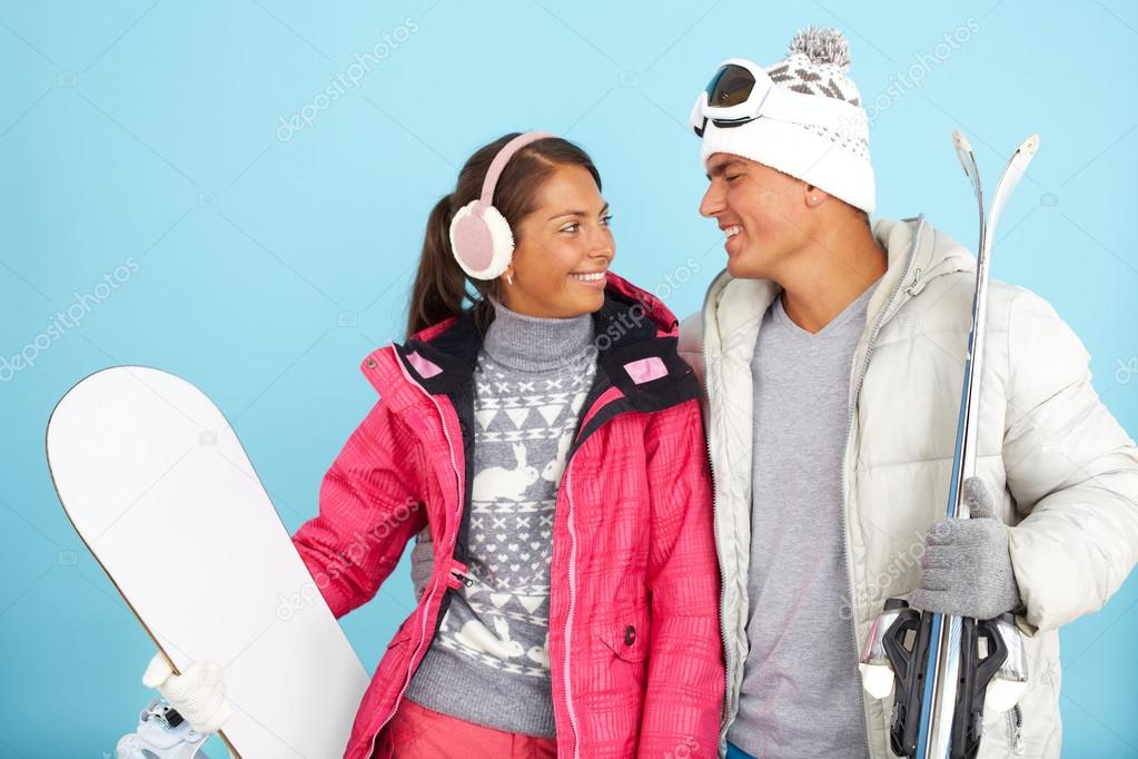Couple holding snowboard and skis