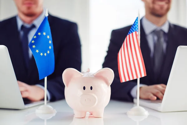 Banco porquinho entre bandeiras da UE e americanas — Fotografia de Stock