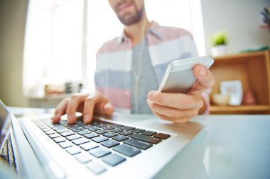 Smartphone kullanarak ve dizüstü bilgisayarda yazarak adam