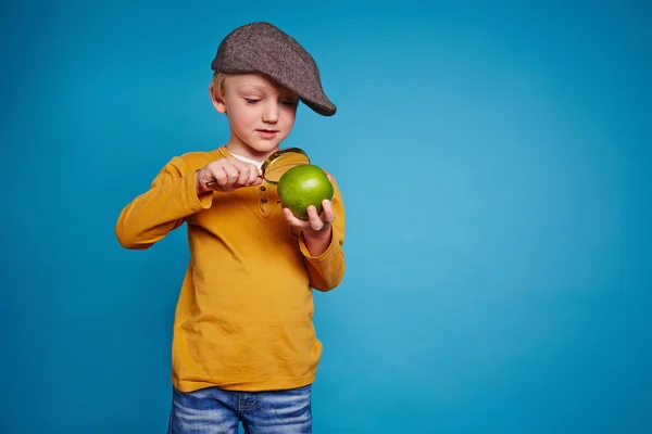 Scolaro guardando mela attraverso lente di ingrandimento — Foto Stock