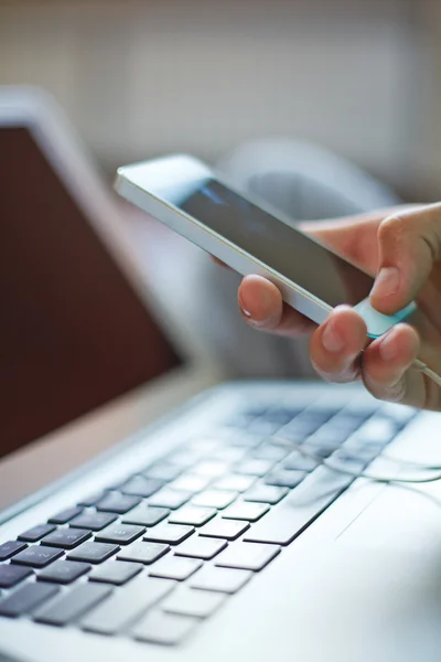 Smartphone in male hand near laptop — Stock Photo, Image