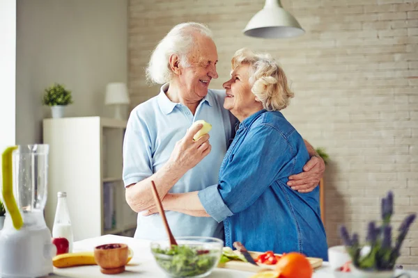 Couple aîné embrassant par table de cuisine — Photo