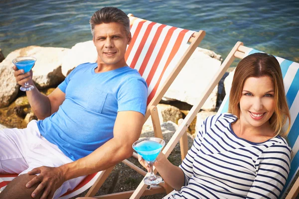 Couple with cocktails sitting on deckchairs — Stock Photo, Image
