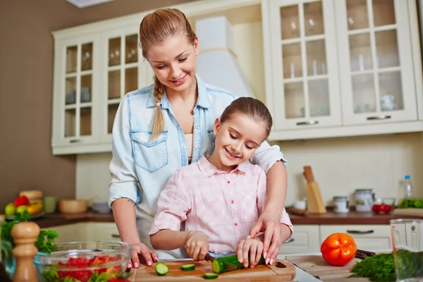 Girl cutting cucumber with mother — Stock Photo, Image