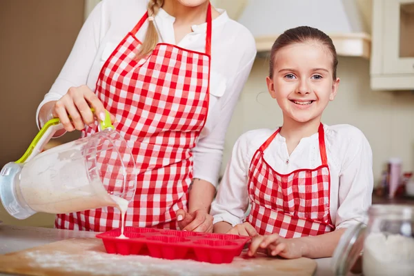 Mãe preenchendo formas de bolinho com massa — Fotografia de Stock