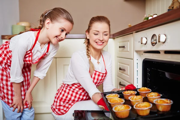 Chica y madre sacando magdalenas del horno — Foto de Stock