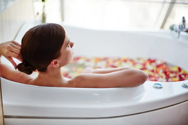 Mujer sentada en baño con pétalos de rosa — Foto de Stock