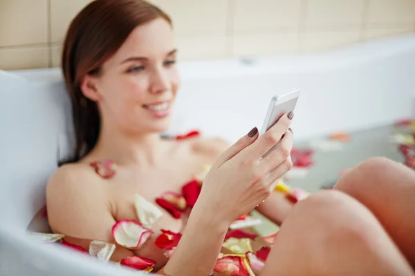 Mujer acostada en el baño y usando teléfono inteligente —  Fotos de Stock