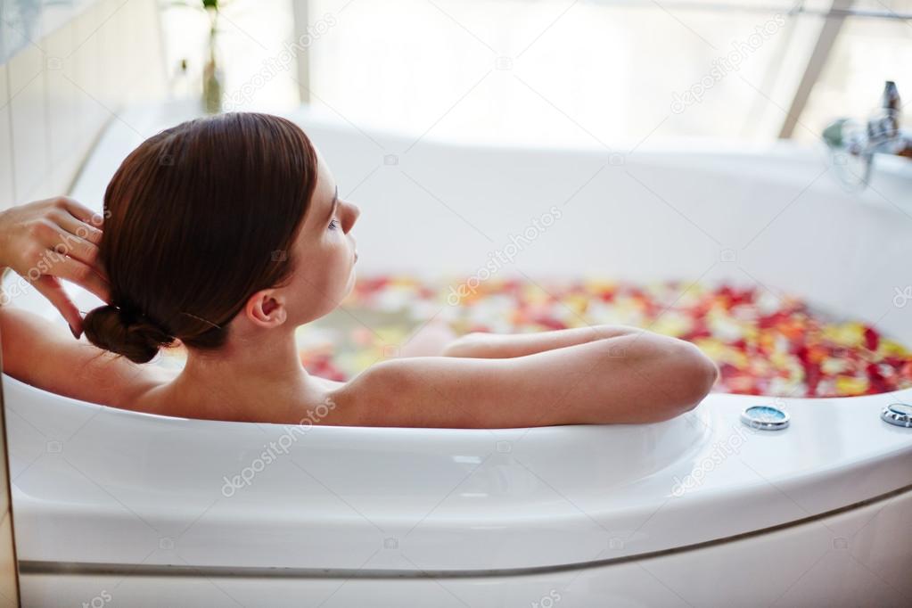 woman sitting in bath with rose petals