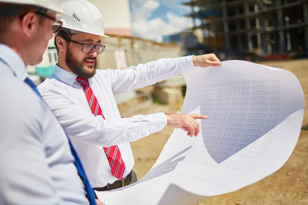 Architects in helmets discussing blueprint — Stockfoto