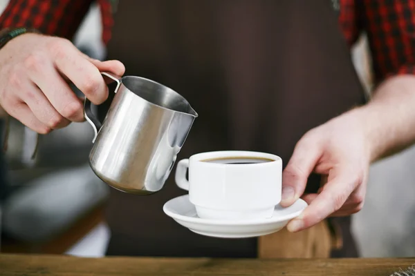 Barista adicionando leite no café preto — Fotografia de Stock